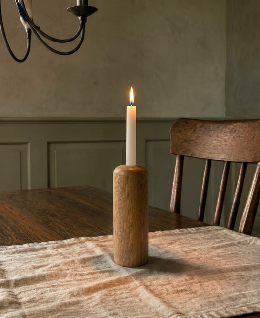 Portavelas Alba encendido sobre una mesa de comedor de madera, con la pared en verde oliva al fondo