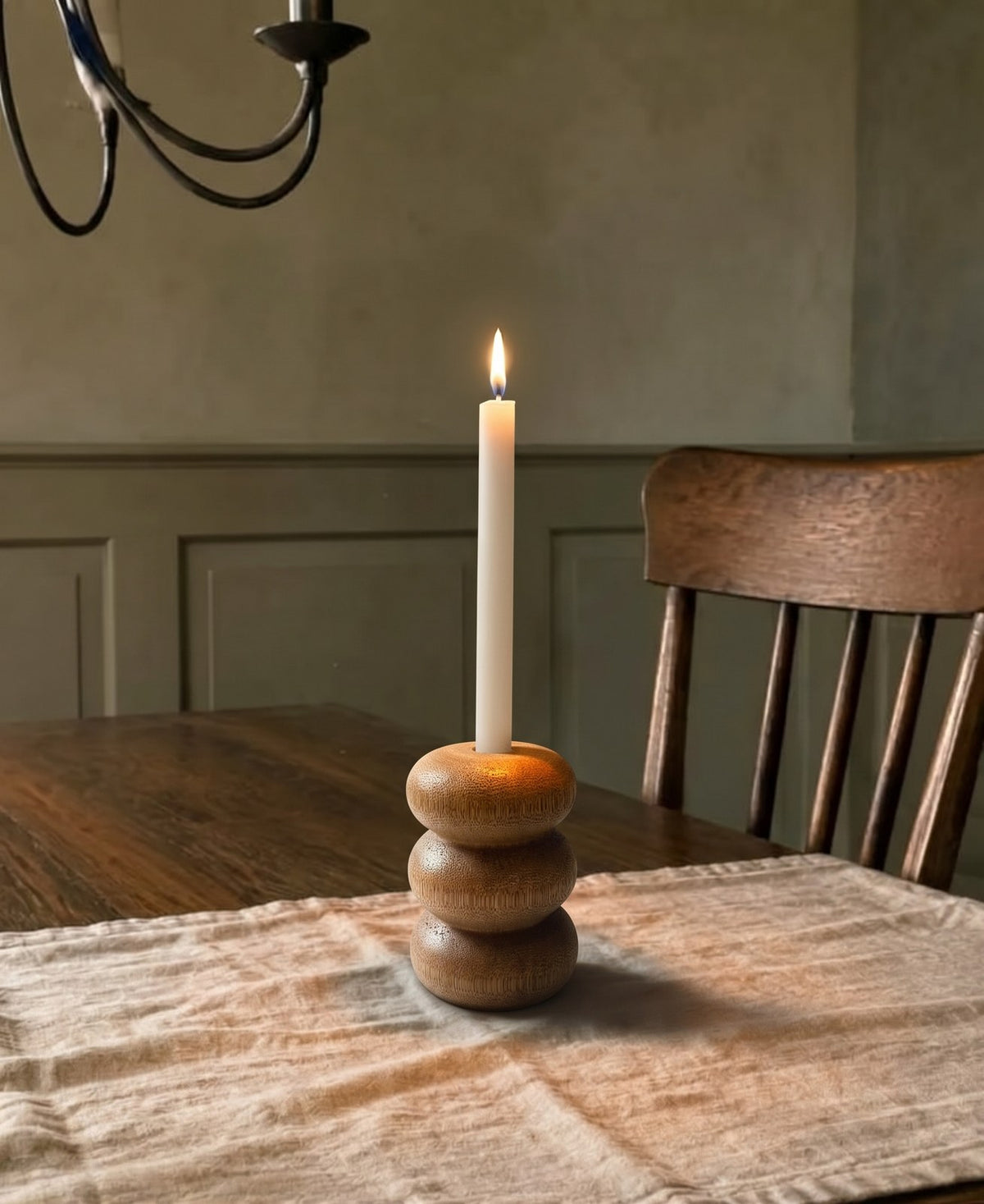 Portavelas Bruna encendido sobre una mesa de comedor de madera, con la pared en verde oliva al fondo