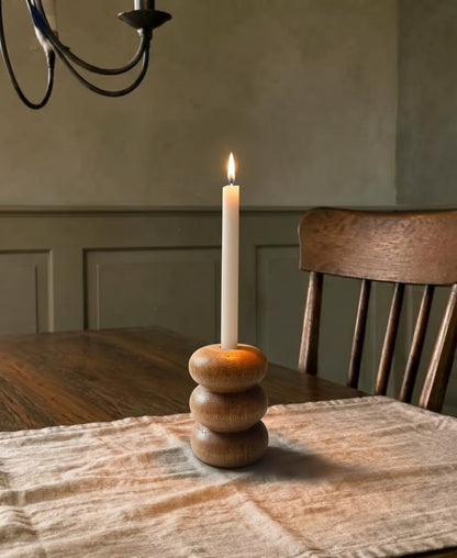 Portavelas Bruna encendido sobre una mesa de comedor de madera, con la pared en verde oliva al fondo