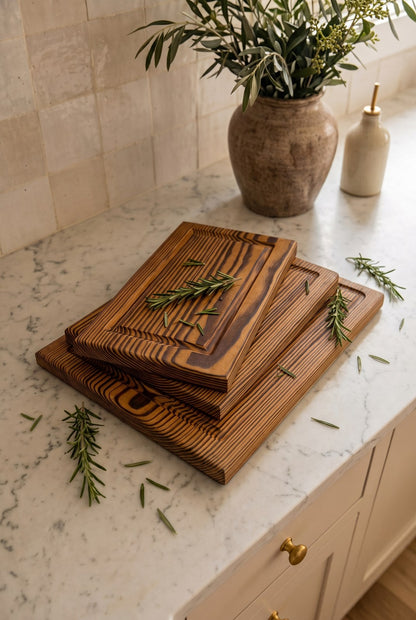 Las tres tablas del kit de PuraMadera apiladas sobre el mesón de la cocina, con romero fresco al lado