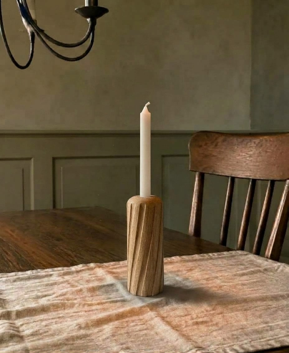 Portavelas Luma encendido sobre una mesa de comedor de madera, con la pared en verde oliva al fondo