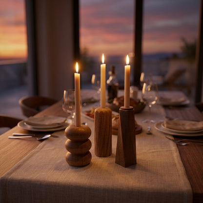 Varios portavelas de PuraMadera encendidos sobre una mesa puesta, con el atardecer por la ventana